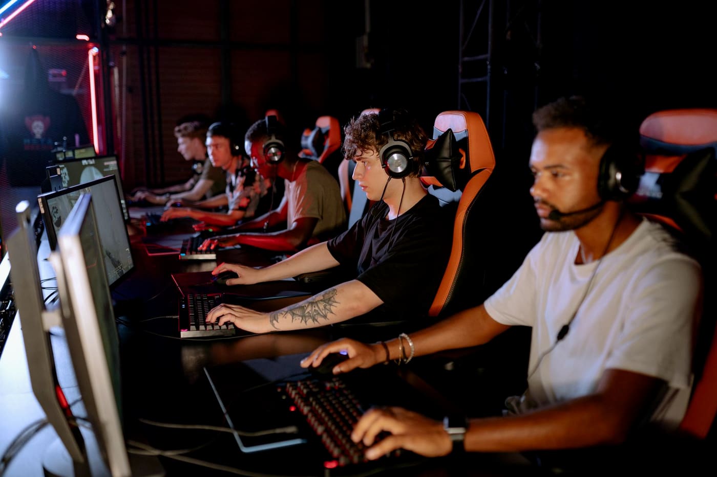 A row of players at gaming stations in a dark, neon-lit gaming space